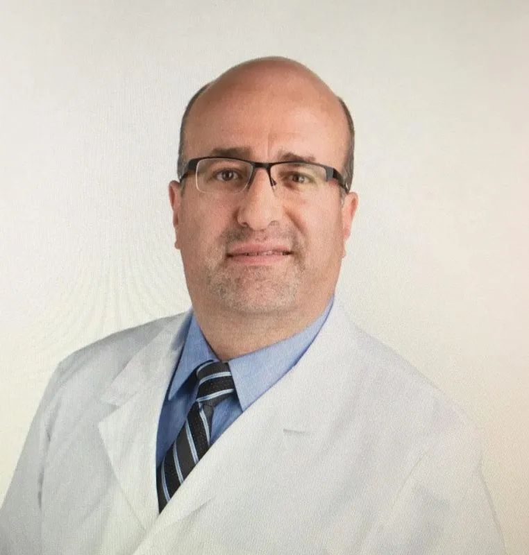 Dr. Maen Haddadin, smiling in white coat, standing in a clinic office in Omaha Nebraska. 