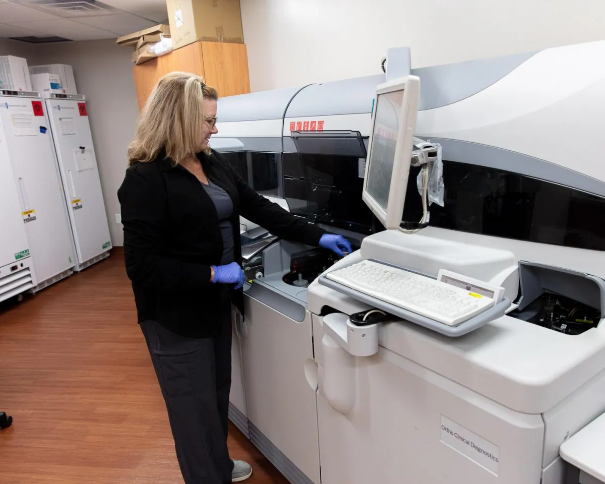 A female doctor, wearing a white lab coat, consults with a young female patient who is seated on an exam table. The patient has one hand on her shoulder, suggesting a potential area of concern, and is looking intently at the doctor. The doctor is gesturing with open hands, engaged in an empathetic conversation. This image highlights the importance of women's wellness exams and access to comprehensive healthcare services in Omaha. Regular check-ups are crucial for early detection and prevention of health issues, ensuring women receive the personalized care they need to maintain their well-being.