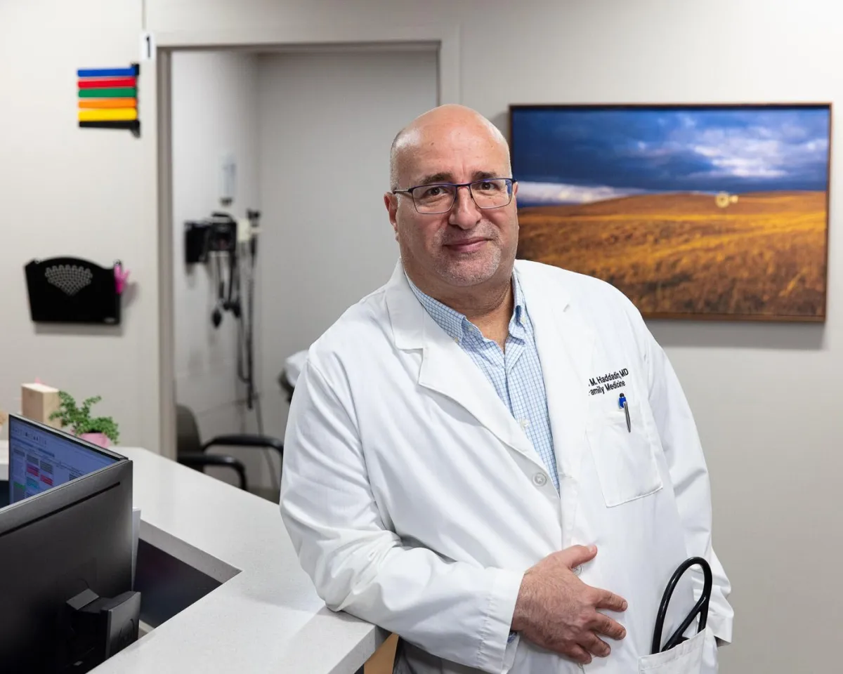 Dr. Maen Haddadin, smiling in white coat, standing in a clinic office in Omaha Nebraska. 
