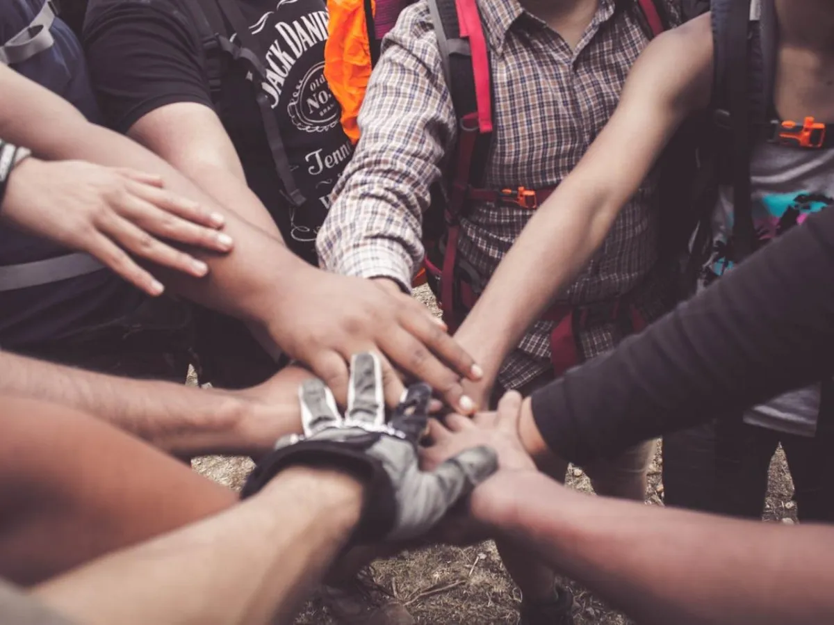 Verschiedene Menschen legen ihre Hände zusammen, repräsentiert Teamarbeit und den gemeinschaftlichen Erfollg bei sozialen Projekten von Gain Freedom.