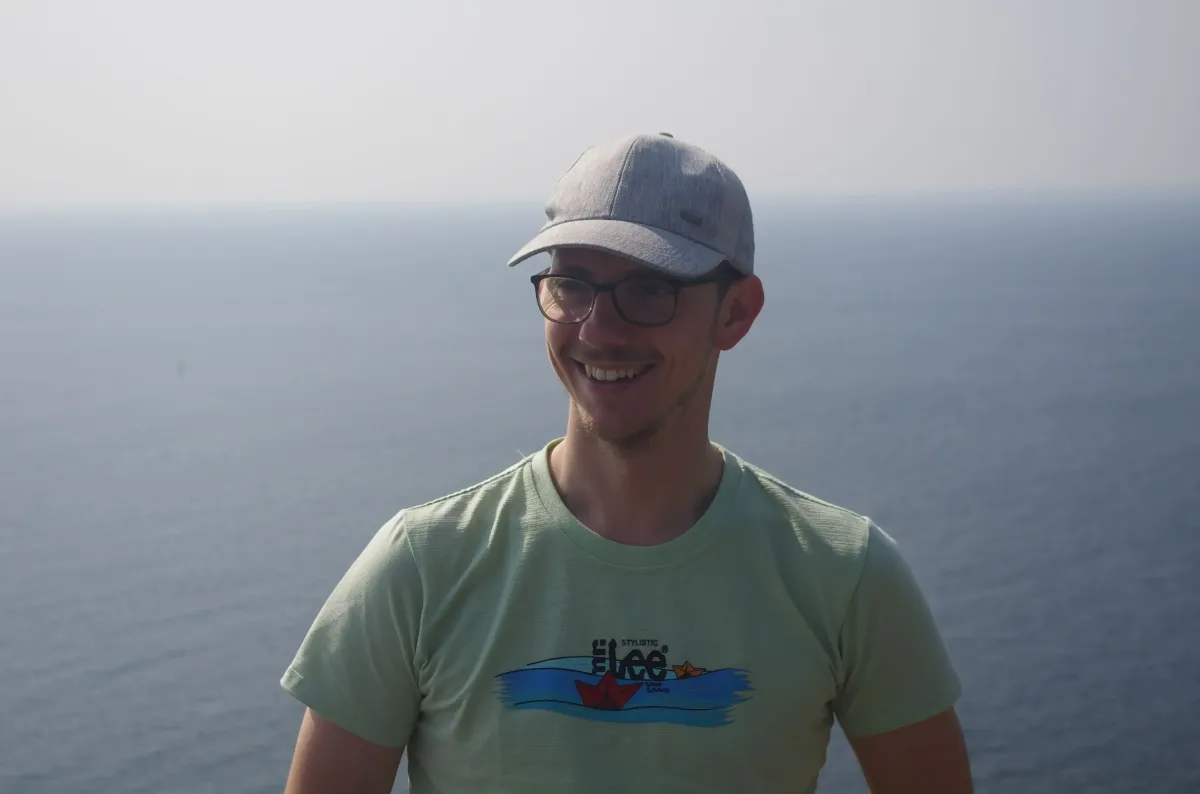 Jan Stracke, Gründer von Gain Freedom, lächelnd mit Kappe vor einer Küstenlandschaft. Über Jan und seine Reise zur finanziellen Freiheit auf der Seite ‚Über uns‘ von Gain Freedom.