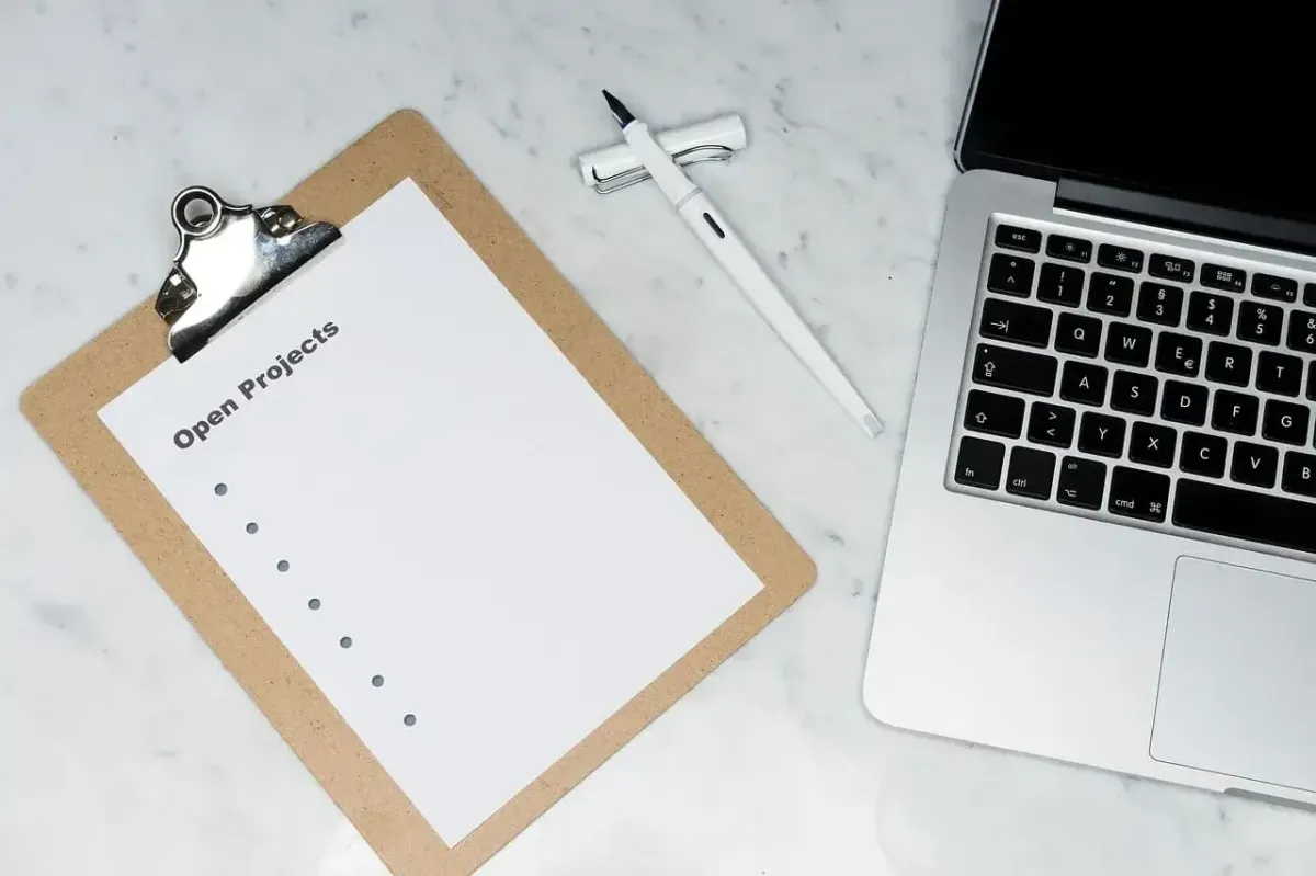 Klemmbrett mit Notiz 'Open Projects' und Laptop, steht für laufende Projekte und Initiativen zur Unterstützung sozialer Zwecke mit Gain Freedom.