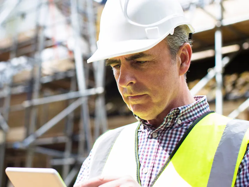 Contractor with hard hat looking down at tablet on a jobsite