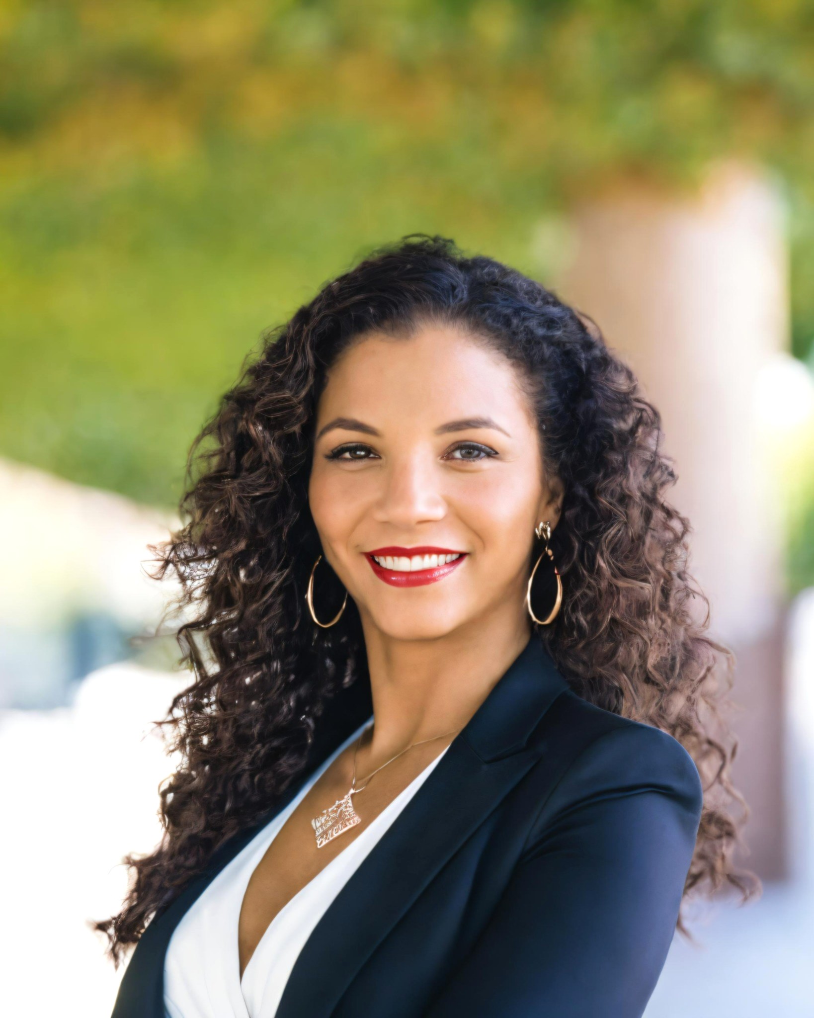 A diverse team of three real estate professionals, two women and one man, are seated at a modern office table with laptops and paperwork. The office has large windows with city views, and the team is smiling, ready to assist clients.