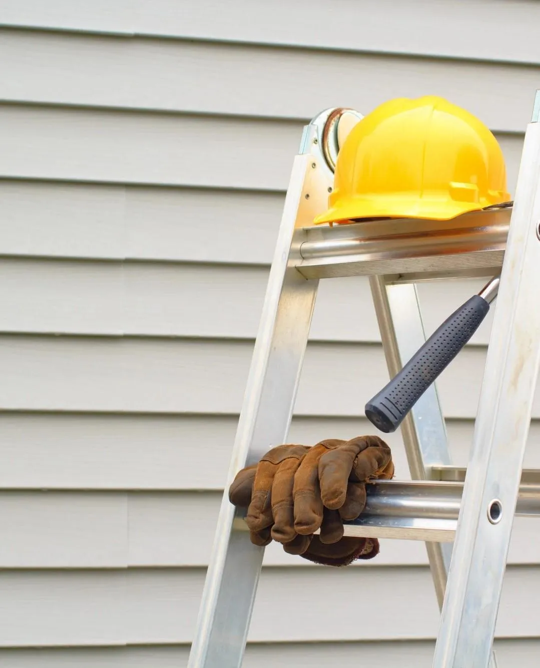 a white siding with a ladder with helmet and gloves