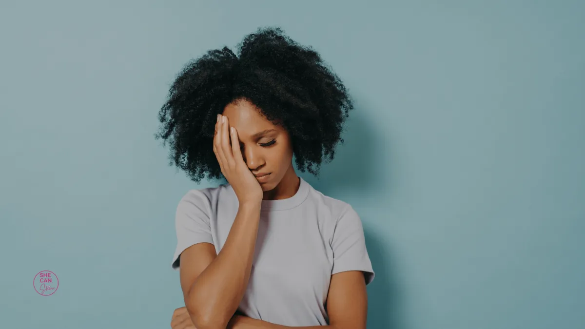 woman with closed eyes looking sad and holding one hand to her face. Blue background.