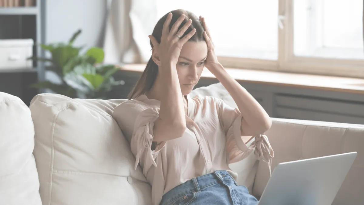 woman holding her hands to her head a a laptop, looking frustrated.