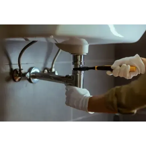 Licensed plumbing technician performing secondary line cleaning on a kitchen sink drain to remove grease and soap scum buildup.
