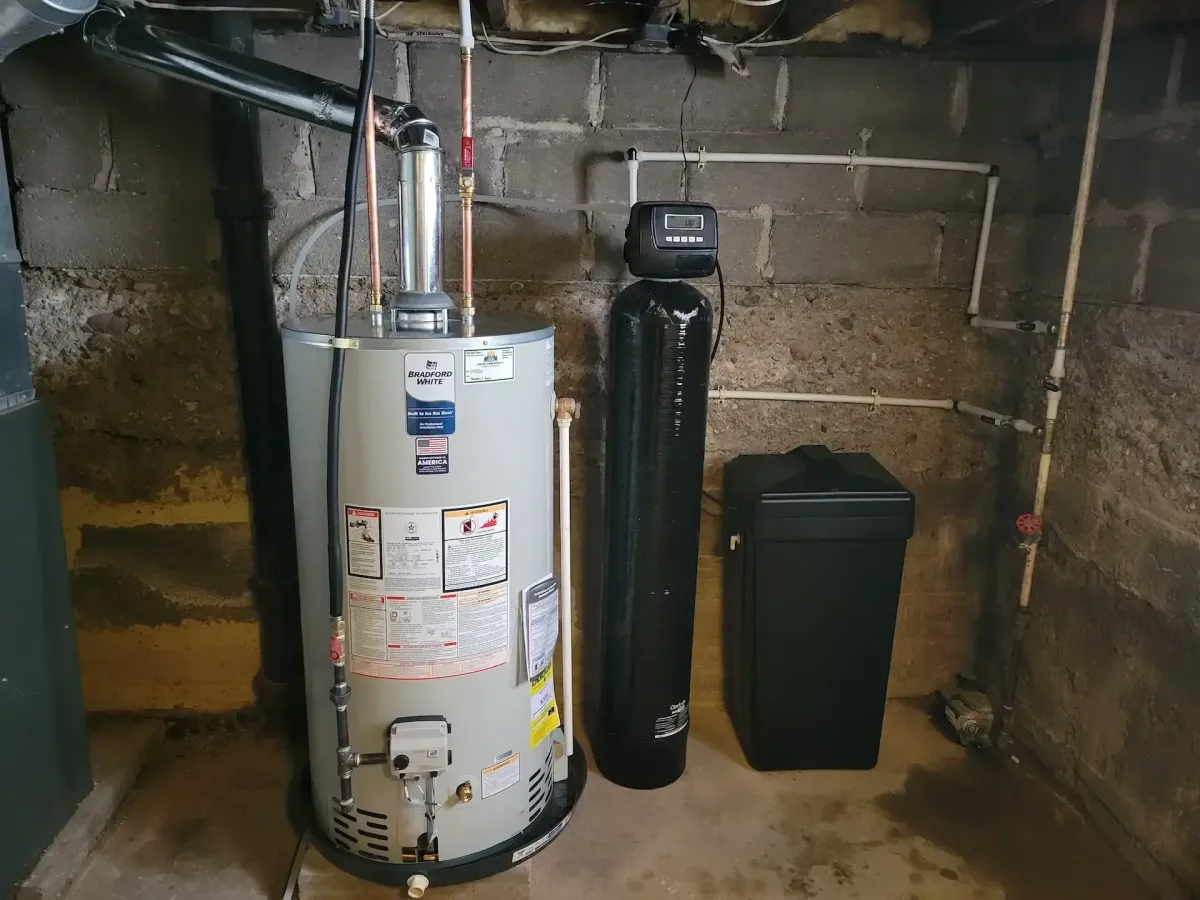 Professional installation of a Bradford White traditional tank water heater and water softening system in a residential basement.