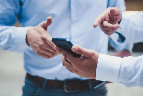 Two professionals talking with each other, holding a mobile phone.