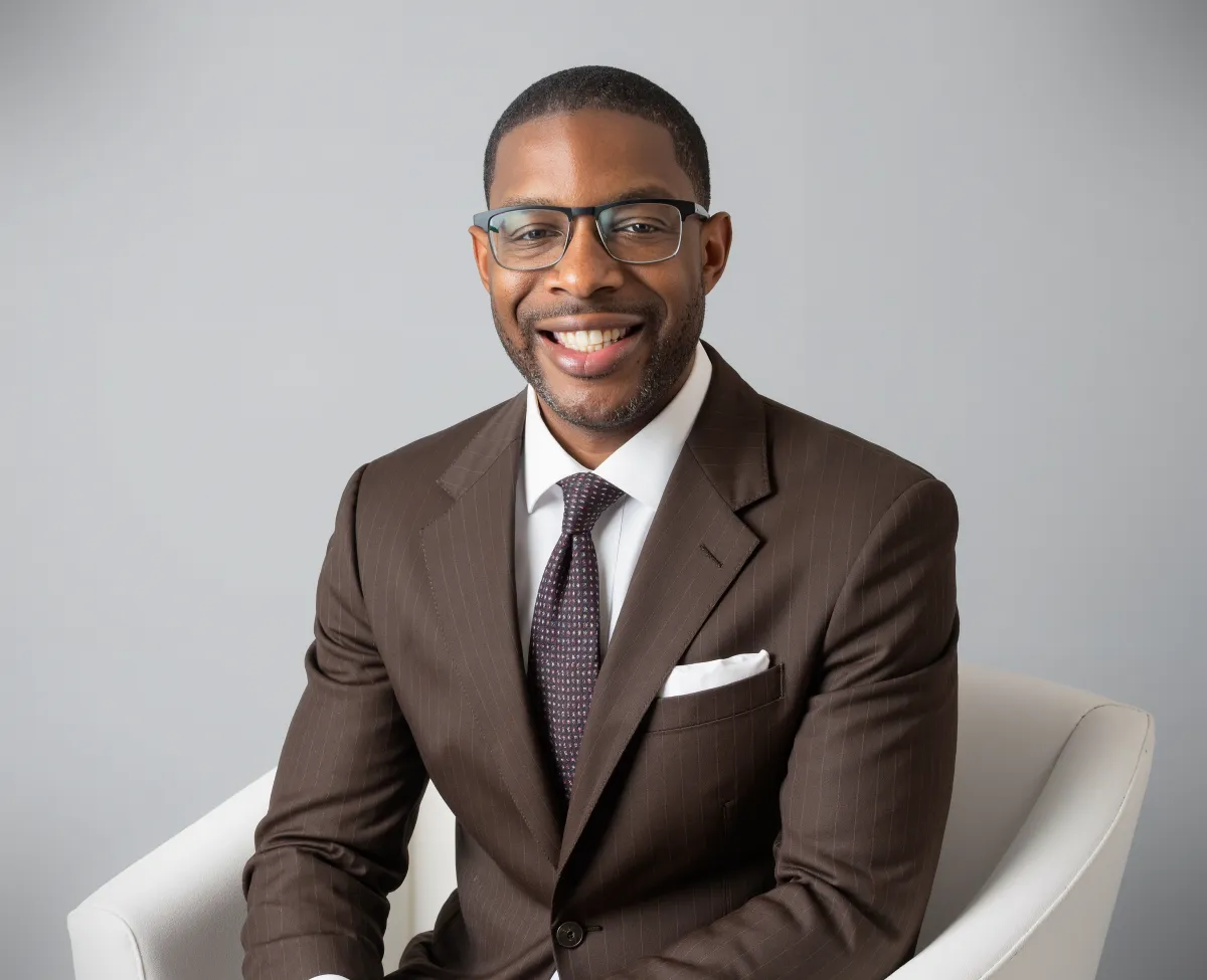 Eugene Robinson, dressed in a tailored navy suit, sits at a polished desk with financial reports and a laptop. His expression is approachable and confident, reflecting years of experience at top financial institutions.