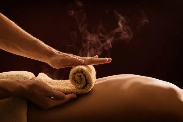 Hands apply a steaming hot towel to a person's back.