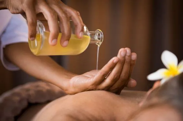 A therapist's hand rests on a client's back as they pour oil into it