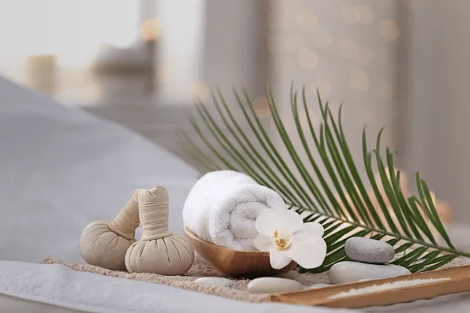 2 Thai poultices next to a clean towel, orchid flower, stones and a large green leaf.