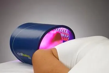 A person laying down with their head inside a light therapy unit. The light glows purple and magenta.