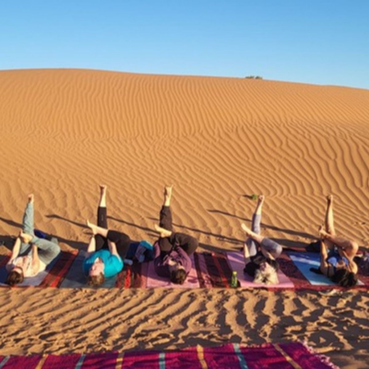 Yoga-Gruppe auf bunten Matten in den Sanddünen der Sahara, Marokko