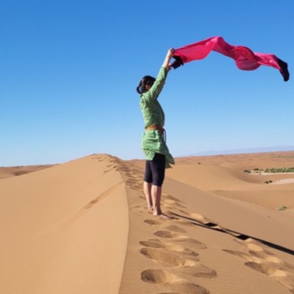 Frau mit rotem Tuch im Wind auf einem Dünenkamm in der Sahara