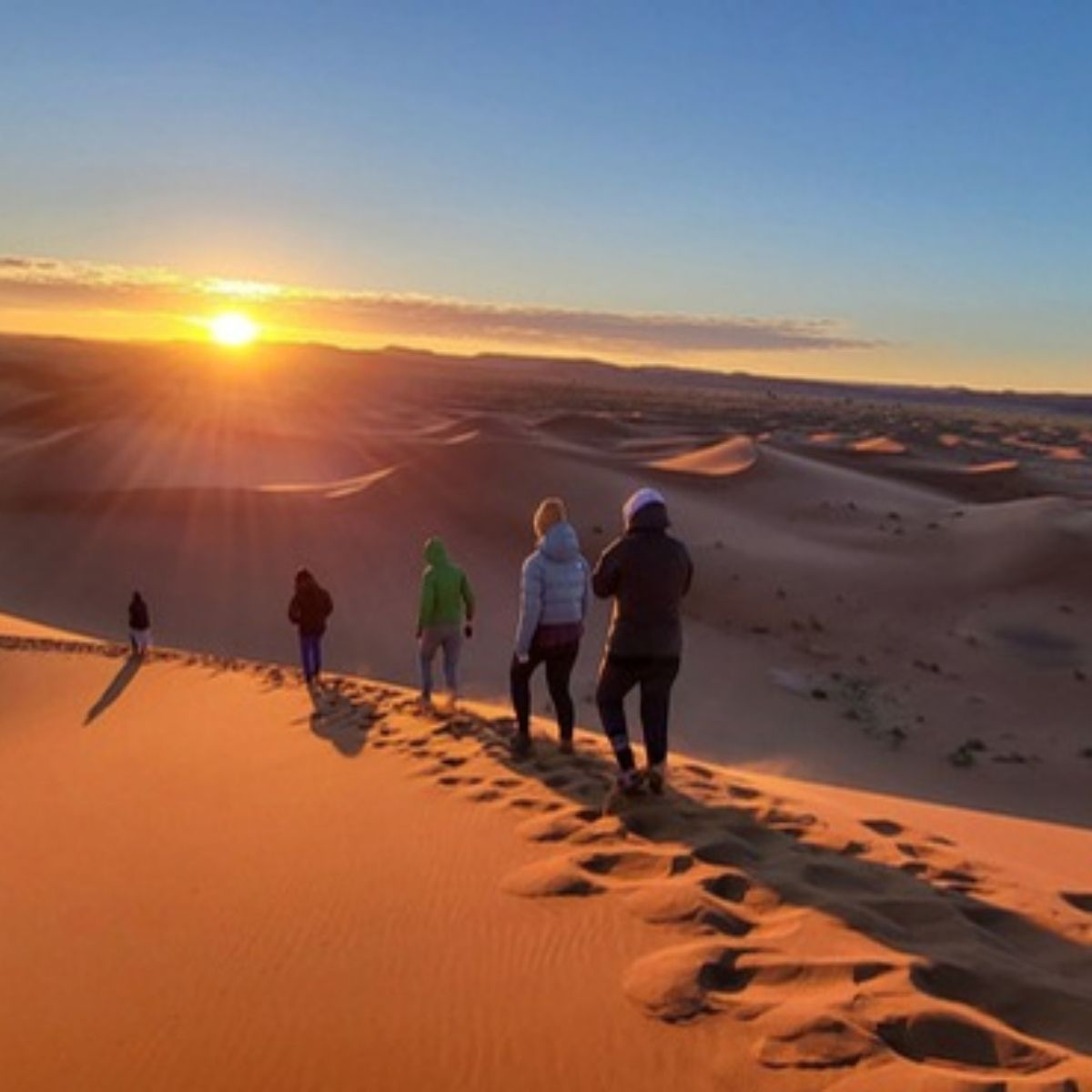 Gruppe wandert bei Sonnenaufgang über eine Düne in der Sahara