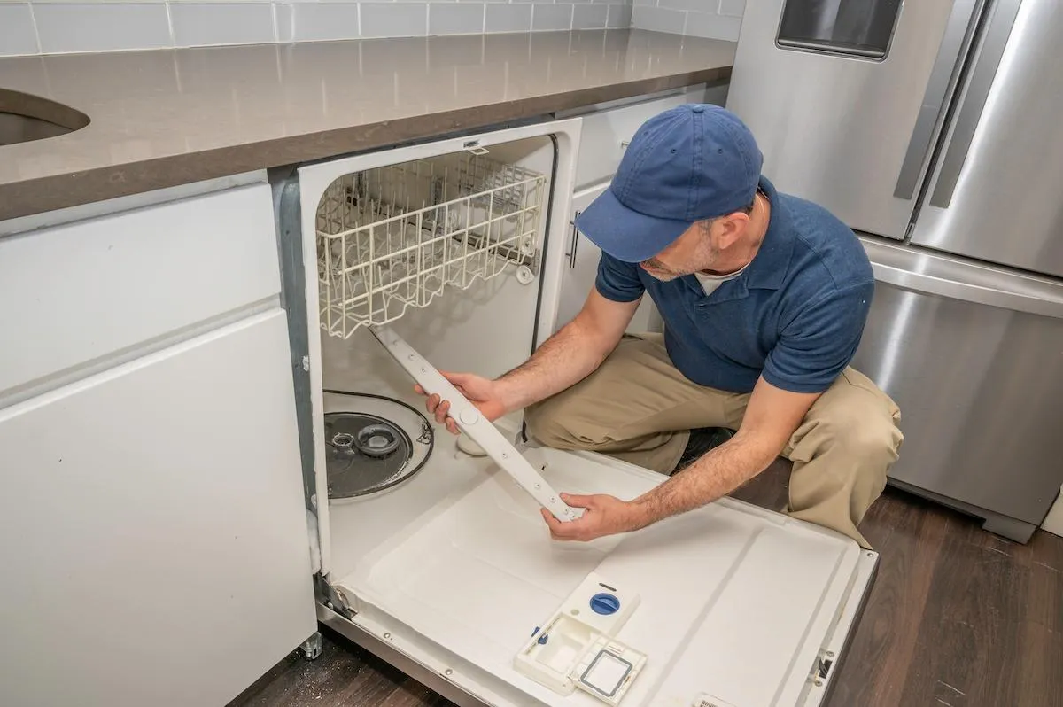 Dishwasher repair technician working under kitchen counter