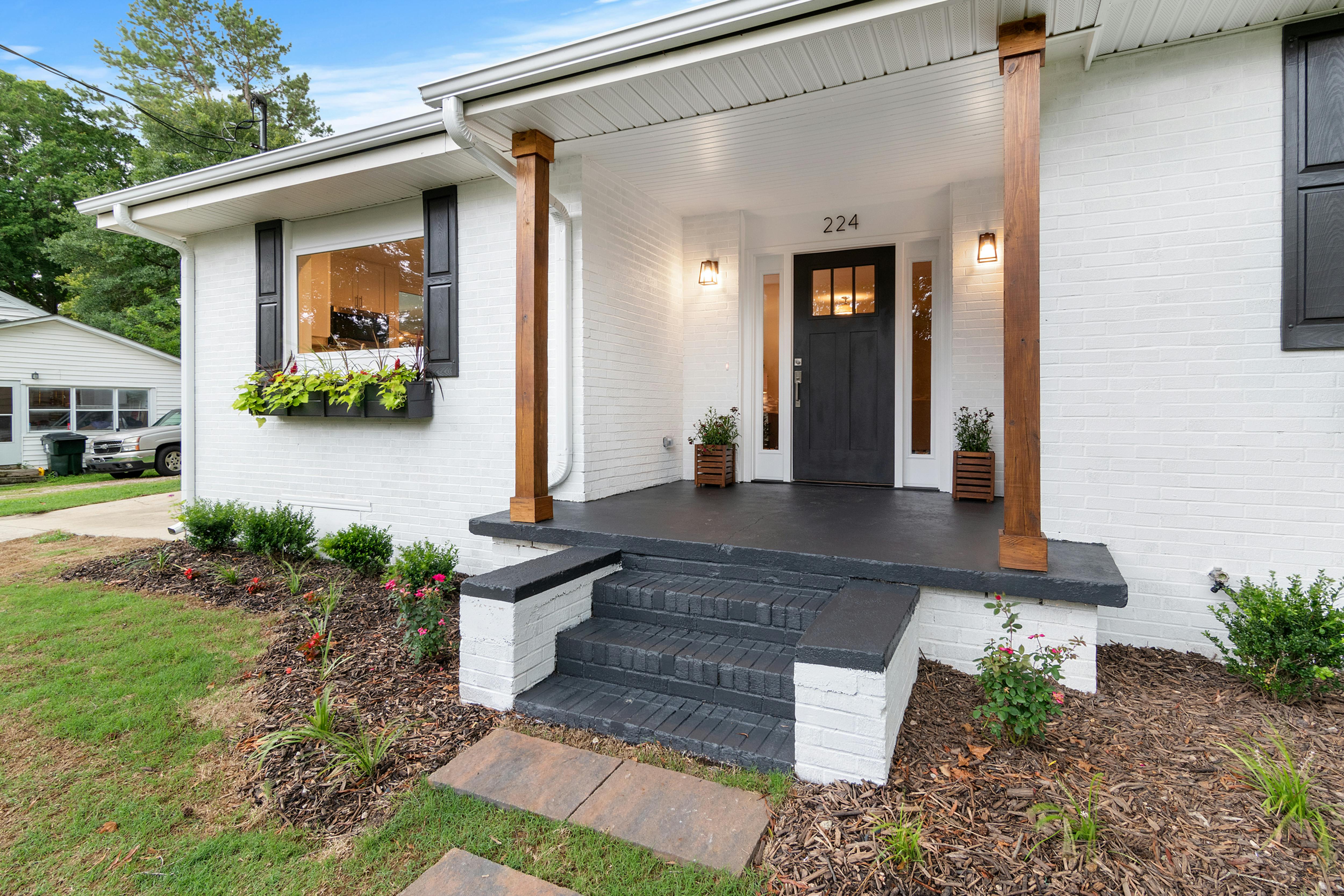 white house with black shutters and porch neatly landscaped 