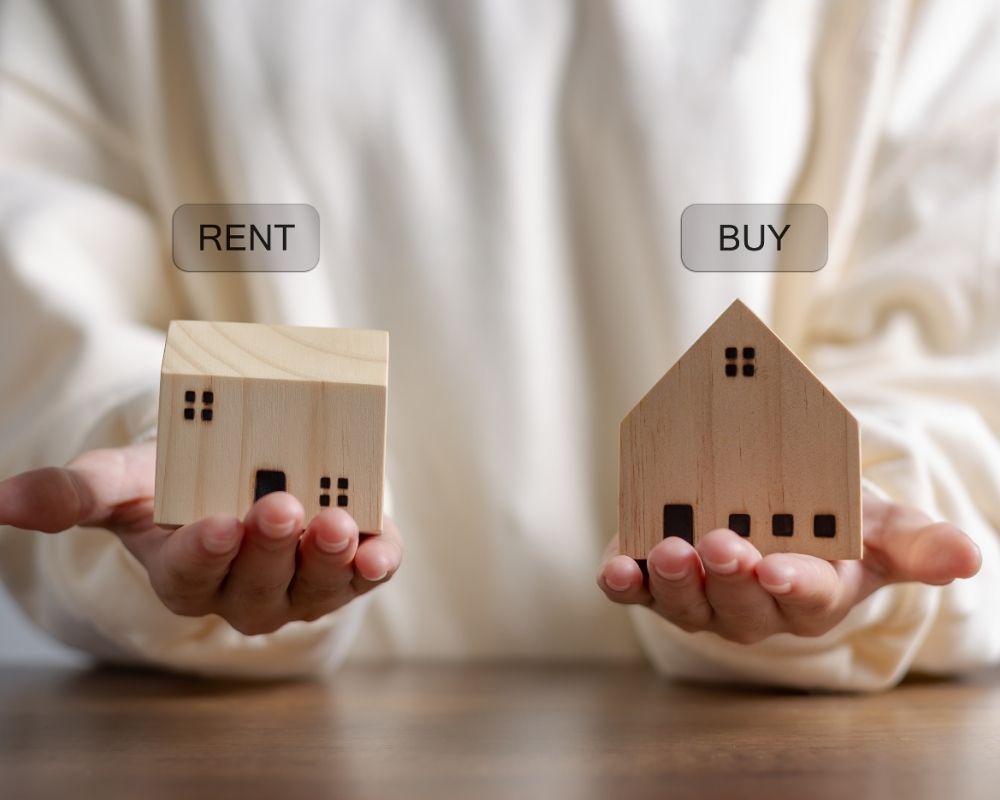 two hands each holding a small wooden home weighing rent vs buying