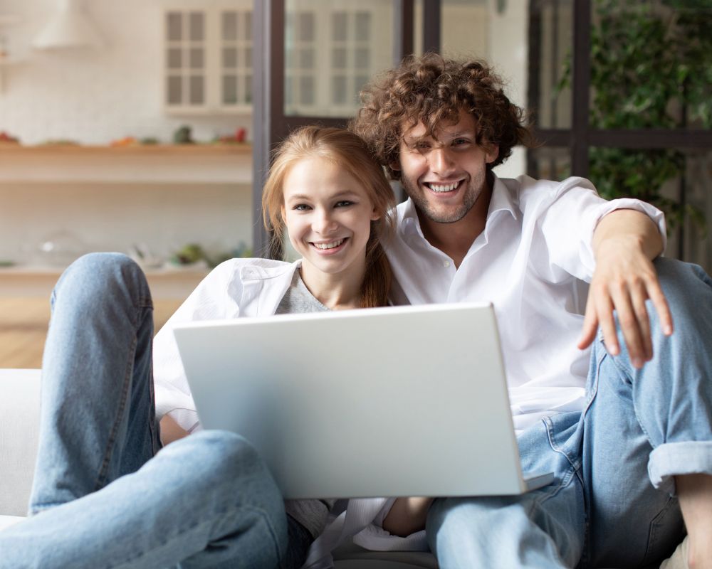 smiling couple sitting on the floor looking at a laptop