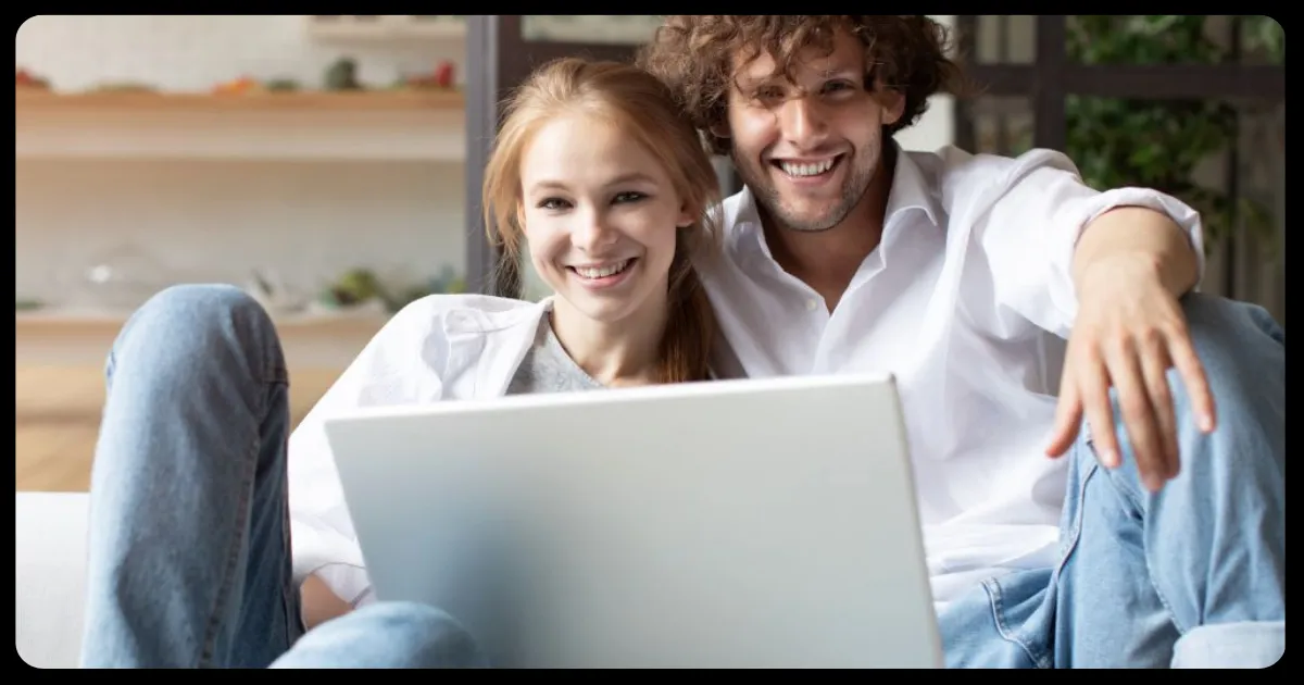 smiling couple sitting on the floor looking at a laptop