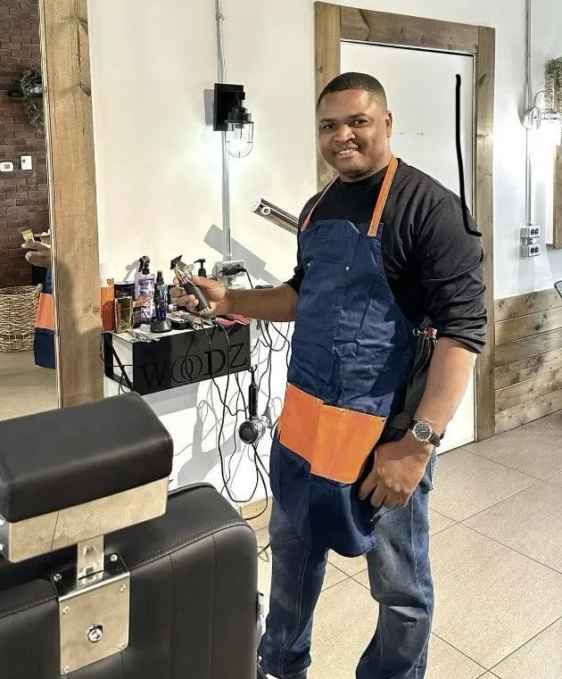 Barbier souriant dans son salon, prêt à accueillir ses clients.