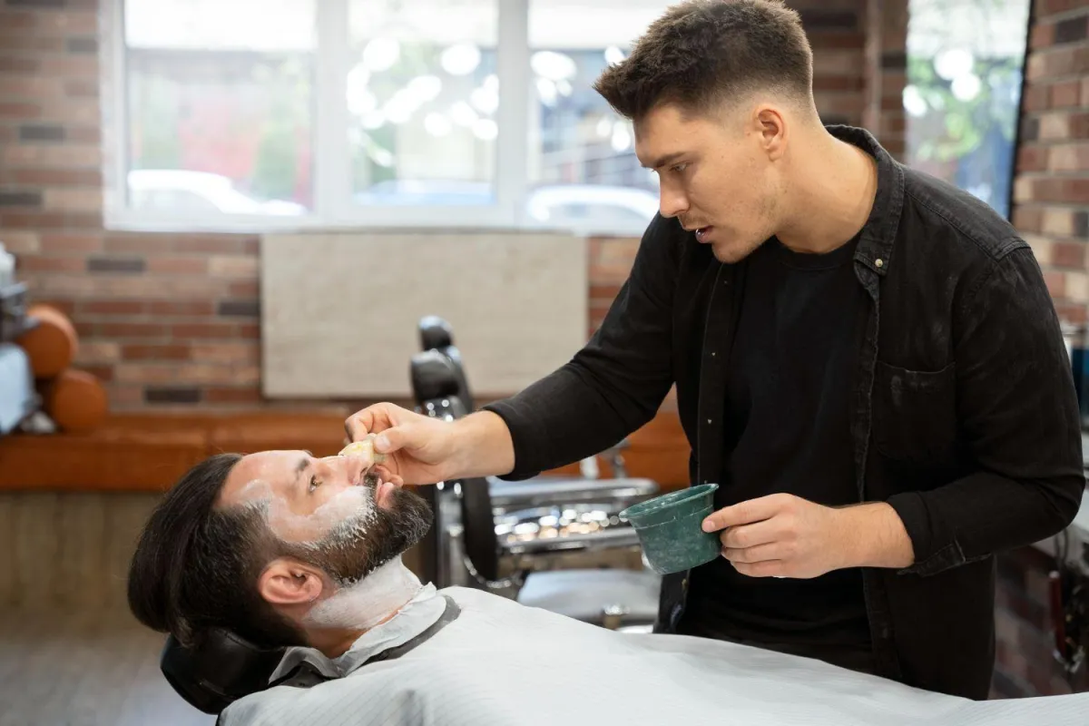 Barbier effectuant un rasage traditionnel avec précision, mettant en avant le savoir-faire classique.