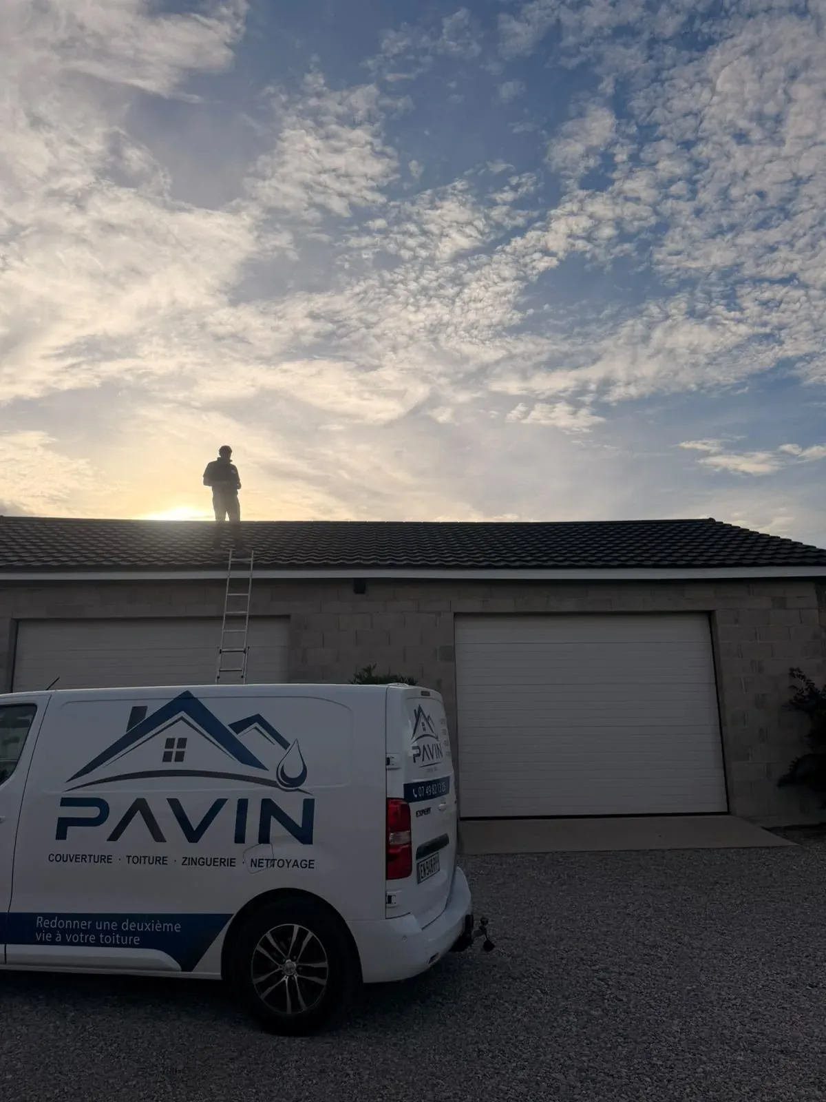 Couvreur Pavin Couvreur sur une toiture à contre-jour près de Beaurepaire, utilitaire en contrebas