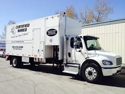 A white shredding truck is parked in front of a building.