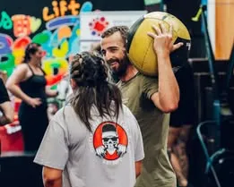 Man and woman performing kettlebell swings in gym.