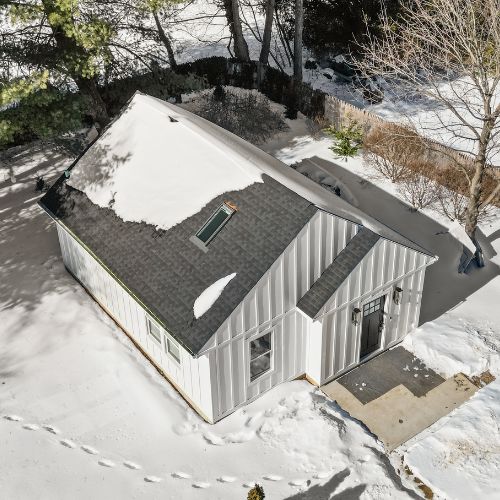 Aerial view of a white detached ADU with a dark roof, surrounded by snow-covered ground and trees in a quiet residential setting.