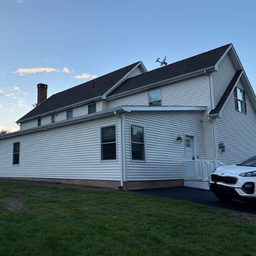 White residential home exterior with an attached ADU-style addition, black roof, paved driveway, and grassy yard under a clear blue sky.