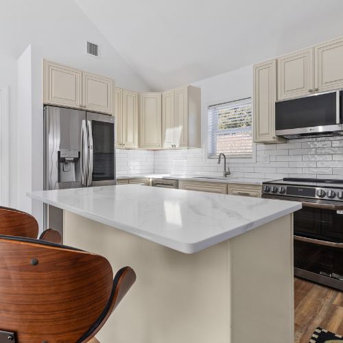 Modern ADU kitchen with cream cabinets, stainless steel appliances, white subway tile backsplash, and a large white island countertop in a bright, open layout.