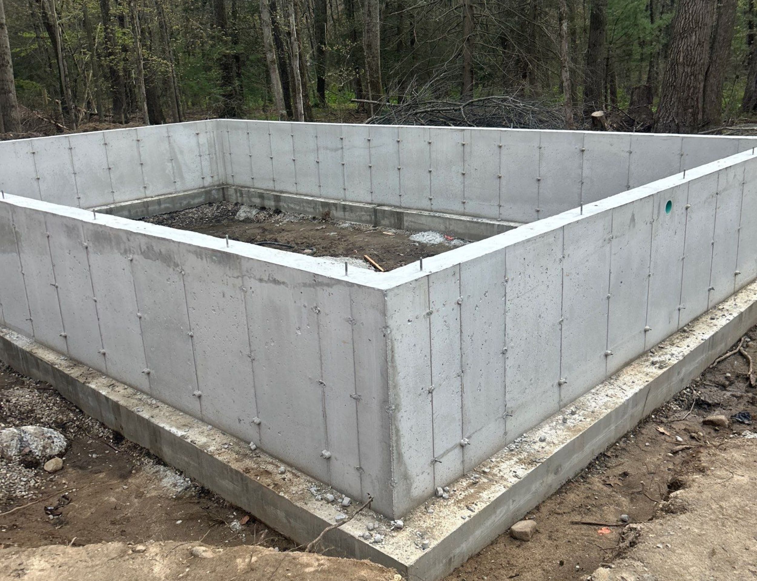 ADU concrete foundation walls under construction at a wooded site.