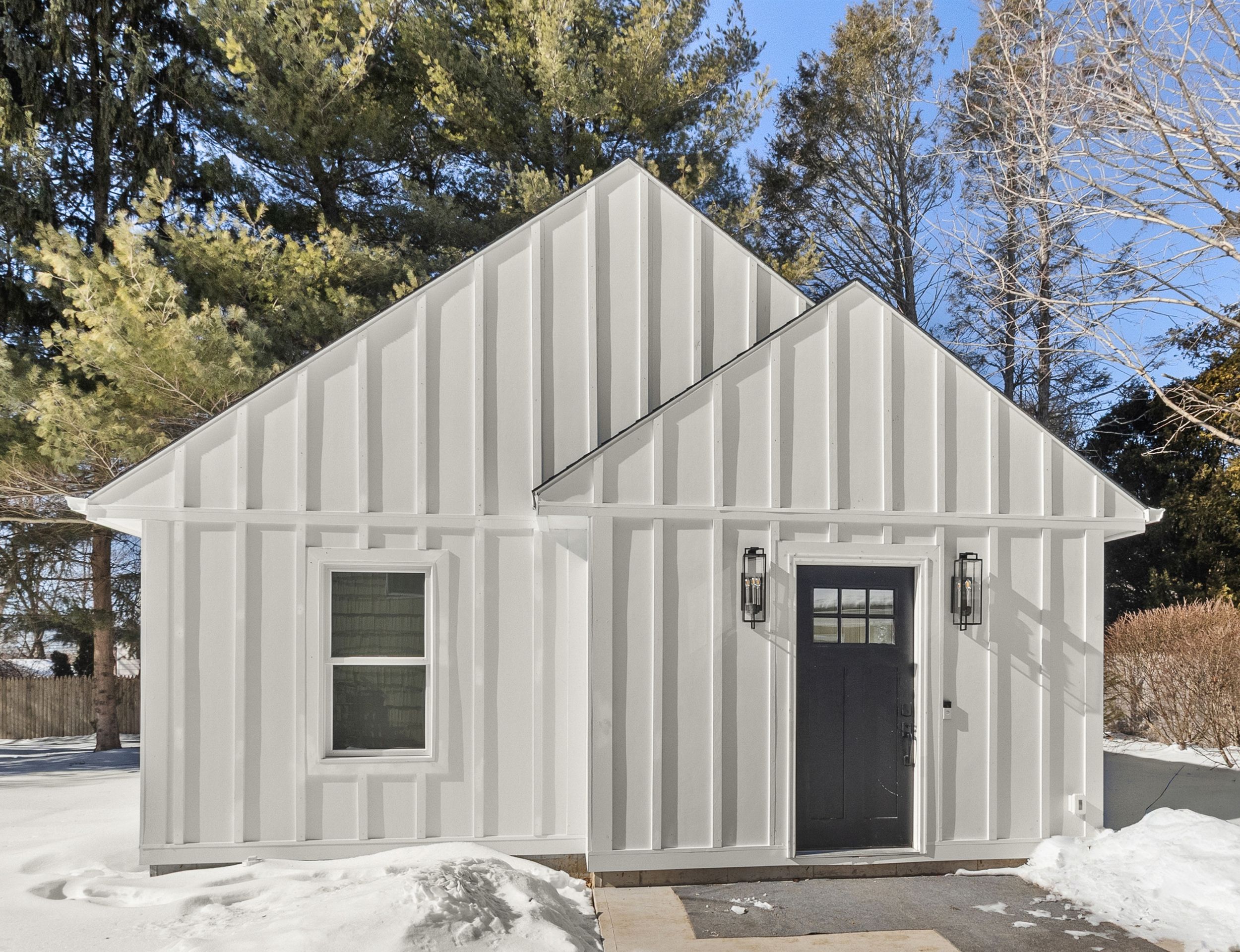 White cottage-style ADU with board-and-batten siding in a snowy yard.