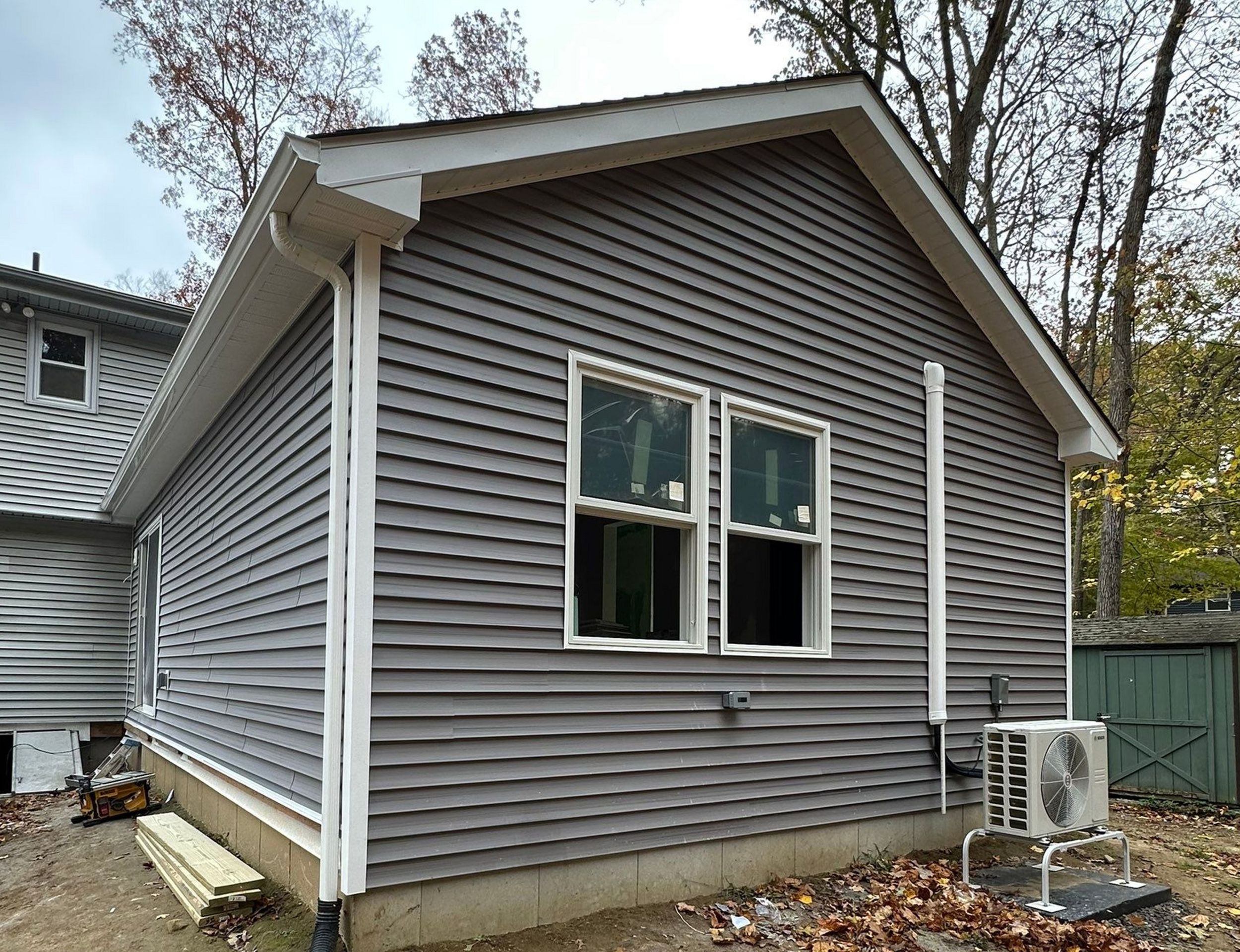 Gray-sided ADU exterior with windows, gutters, and an outdoor HVAC unit.