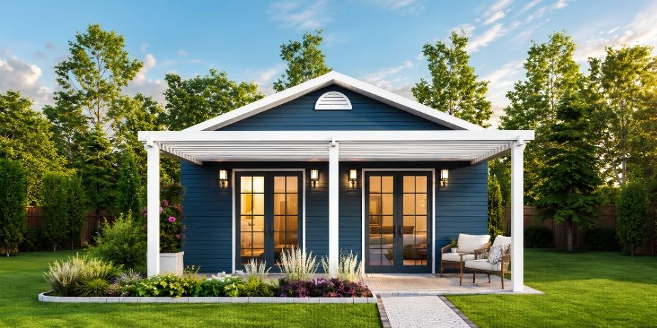 Blue single-story Connecticut ADU with white trim, a covered front porch, French doors, landscaped garden beds, and a manicured lawn.