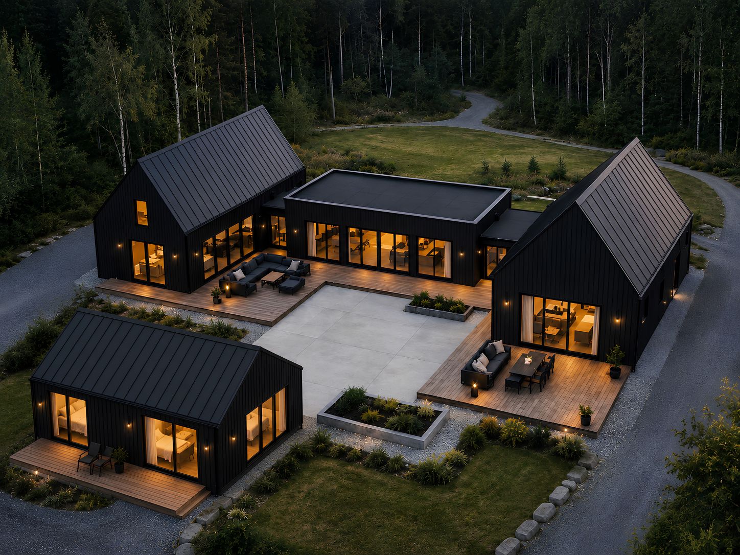 Aerial view of a modern black-clad ADU compound with four connected and detached structures, warm interior lighting, private decks, and a central courtyard surrounded by forest.