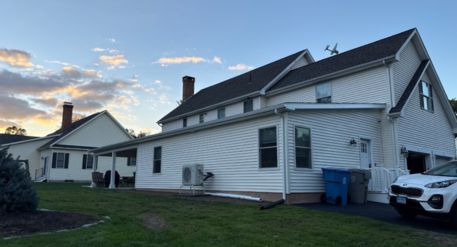 Exterior of a white Connecticut home with an attached ADU, dark roof, lawn, driveway, and parked vehicle at sunset.