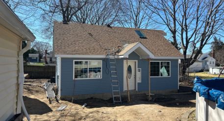 Blue backyard ADU under construction with ladders, new siding, front windows, entry door, and a small gabled roof.