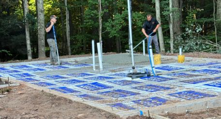 Workers prepare a concrete foundation slab with radiant heating tubing and plumbing lines for a new ADU.