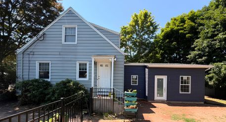 Attached ADU Light blue Connecticut home with a dark blue attached ADU addition, separate entrance, windows, and fenced walkway.