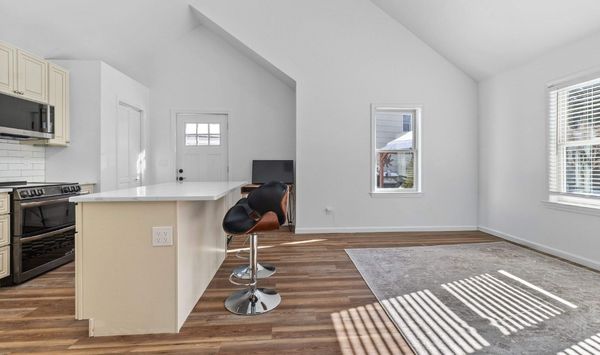 Bright ADU interior with a vaulted ceiling, compact kitchen, breakfast bar, wood flooring, and sunlit living area.