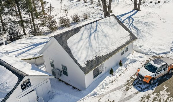 Aerial winter view of a completed white backyard ADU with a snow-covered roof and a construction truck parked beside it.
