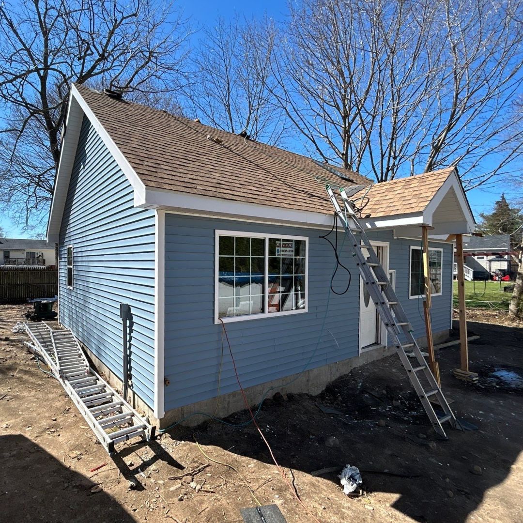 Blue backyard ADU under construction with ladders, new siding, windows, and roofing work in progress.
