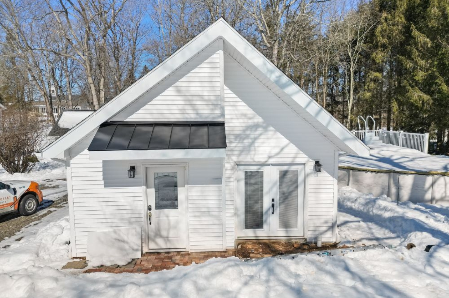 White detached ADU with a steep gable roof surrounded by snow in Guilford, Connecticut.
