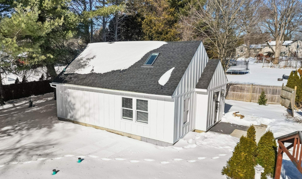 Detached accessory dwelling unit in a Connecticut backyard during winter, featuring white siding, a pitched dark roof, skylight, and snow-covered surroundings.