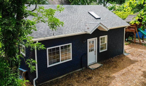 Wood-framed ADU under construction with exterior sheathing, roof rafters, window openings, and a worker on a lift.